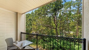 Un balcone con tavolo e sedie che si affaccia su un giardino alberato sotto un cielo sereno.