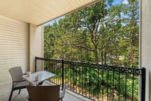 Ein Balkon mit Tisch und Stühlen, Blick auf einen Garten mit Bäumen und blauem Himmel.