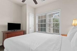 Ein Hotelzimmer mit einem Bett, einem Fernseher auf einer Holzkommode, einem Fenster mit Jalousien und einer Lampe.
