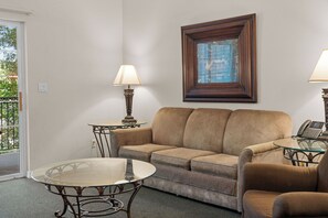 Ein Wohnzimmer mit einer Couch, zwei Beistelltischen, einem Glastisch und einem gerahmten Bild an der Wand.