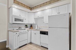 Cocina con gabinetes blancos, microondas, estufa, lavavajillas y refrigerador.