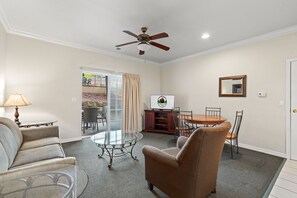 A living room with a glass coffee table, a brown armchair, a television, and a ceiling fan. - Stay Close to the Strip | Pet Friendly Queen Condo (Branson)