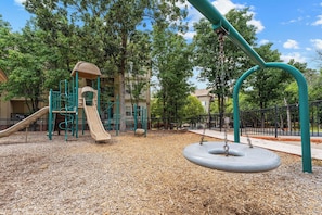 Ein Spielplatz mit Rutsche, Schaukeln und einer Kletteranlage.