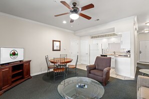 A living room with a ceiling fan, a dining table with chairs, a brown armchair, and a glass coffee table. - Queen Condo Near Highway 76 | Pool & Hot Tub (Branson)