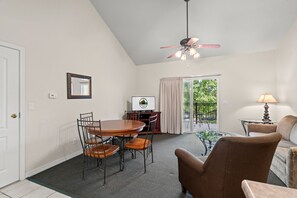 Ein Zimmer mit Esstisch, Stühlen, Deckenventilator, Fernseher und Blick ins Freie.