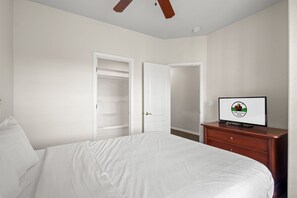 A hotel room with a bed, a wooden dresser, a television, and a closet. - Resort Queen Condo | Balcony • Pool • Hot Tub (Branson)