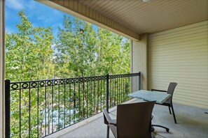 A balcony with a table and chairs, a metal railing, and a view of trees and sky. - Relax at French Quarter Resort | Queen Condo (Branson)