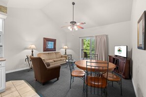 A living room with a sofa, a dining table with chairs, a ceiling fan, and a television. - Relax at French Quarter Resort | Queen Condo (Branson)