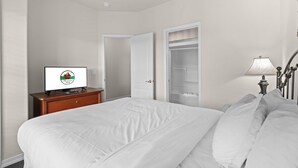 A hotel room with a bed, a desk with a computer, a wardrobe, and a ceiling fan. - Relax at French Quarter Resort | Queen Condo (Branson)