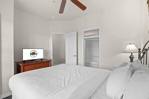 A hotel room with a bed, a desk with a computer, a wardrobe, and a ceiling fan. - Relax at French Quarter Resort | Queen Condo (Branson)
