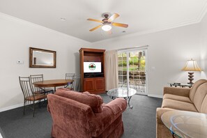 Ein Wohnzimmer mit Deckenventilator, einem Esstisch mit Stühlen, einer Couch, einem Glastisch und einem Fernseher.