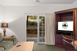 A living room with a television, a sofa, a table, and a sliding glass door leading to a garden. - King Suite | Pet Friendly | Resort Pool & Hot Tub (Branson)