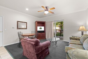 Ein Wohnzimmer mit Deckenventilator, einem Esstisch mit Stühlen, einer Couch und einem Couchtisch mit Glasplatte.