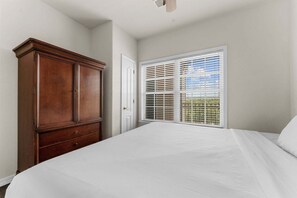 A bedroom with a large wooden wardrobe, a white bed, and a window with blinds. - Stay Near the Branson Strip | King Condo + Pool (Branson)