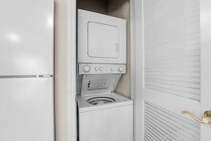 A compact, white laundry room with a built-in washer and dryer, a control panel, and a door with a brass handle. - Stay Near the Branson Strip | King Condo + Pool (Branson)