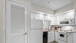 Una cocina con armarios blancos, un refrigerador, un microondas, un lavavajillas y un horno.