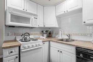 A modern kitchen with white cabinetry, a stove, a microwave, and a sink. - Relaxing King Condo | Close to Shows & Attractions (Branson)