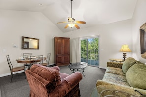 A living room with a dining table, chairs, a sofa, a glass coffee table, a ceiling fan, and a view through a glass door. - Relaxing King Condo | Close to Shows & Attractions (Branson)