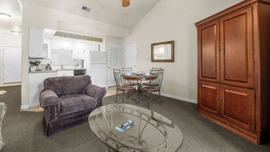 A living room with a sofa, a glass coffee table, a dining table with chairs, a wooden cabinet, and a ceiling fan. - Relaxing King Condo | Close to Shows & Attractions (Branson)