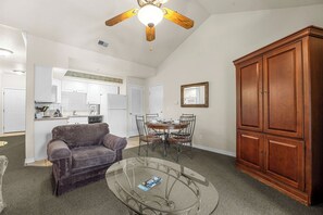 A living room with a sofa, a glass coffee table, a dining table with chairs, a wooden cabinet, and a ceiling fan. - Relaxing King Condo | Close to Shows & Attractions (Branson)