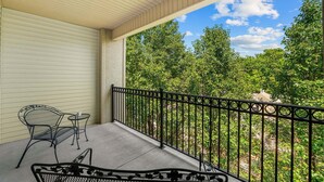 A covered balcony with a metal railing, a chair, and a small table. - Relaxing King Condo | Close to Shows & Attractions (Branson)