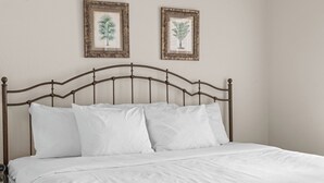 A bed with a metal headboard, white bedding, and two framed botanical prints on the wall. - King Suite | Pet Friendly | Resort Pool & Hot Tub (Branson)