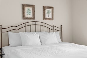 A bed with a metal headboard, white bedding, and two framed botanical prints on the wall. - King Suite | Pet Friendly | Resort Pool & Hot Tub (Branson)