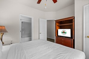 Ein Hotelzimmer mit einem Bett, einem Schreibtisch mit Lampe, einem Kleiderschrank und einem Fernseher, der ein Logo zeigt.