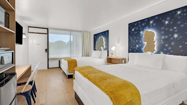 Ein Hotelzimmer mit zwei Betten, einem Schreibtisch, einer Küchenzeile und einem großen Fenster.