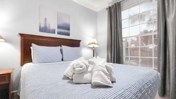 Ein ordentlich bezogenes Bett mit gestreifter Bettdecke und zwei Kissen, eine Nachttischlampe sowie zwei gerahmte Bilder an der Wand.