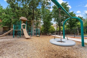 A playground with a slide, swings, and a climbing structure. - King Condo Near the Branson Strip | Pool & Hot Tub (Branson)