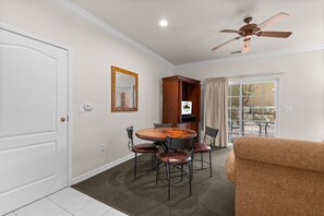 A room with a dining table, chairs, a television, a ceiling fan, and a sliding glass door leading to an outdoor area. - King Condo | Close to Shows & Attractions (Branson)