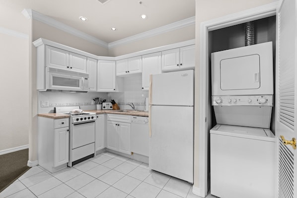 A kitchen with white cabinetry, a stove, a microwave, a refrigerator, and a washing machine. - King Condo | Close to Shows & Attractions (Branson)
