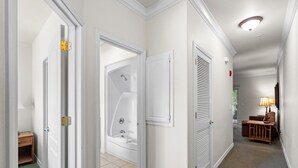 A hallway with a bathtub, a door with a latch, a wall-mounted air vent, and a lamp. - French Quarter King Getaway | Pet Friendly Resort (Branson)