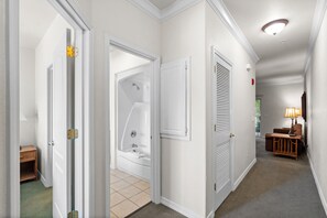 A hallway with a bathtub, a door with a latch, a wall-mounted air vent, and a lamp. - French Quarter King Getaway | Pet Friendly Resort (Branson)