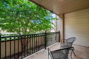 A balcony with a metal railing, two metal chairs, and a view of trees and buildings. - French Quarter King Getaway | Pet Friendly Resort (Branson)