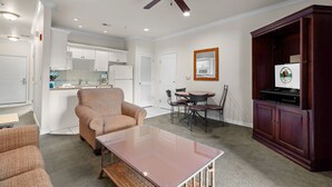 Sala de estar com sofá, mesa de centro, área de jantar com cadeiras, cozinha ao fundo e um ventilador de teto.