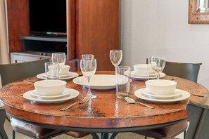 A round dining table set with white plates, bowls, and clear wine glasses, accompanied by cutlery. - King Condo Near Silver Dollar City & Highway 76 (Branson)