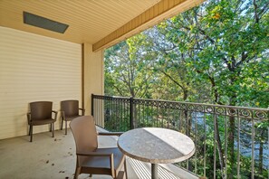 Ein Balkon mit zwei Korbstühlen und einem runden Tisch, mit Blick auf eine dicht bewaldete Gegend.