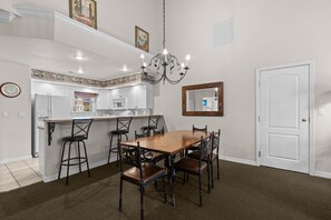 Uma sala de jantar com uma mesa e cadeiras de madeira, uma cozinha com armários brancos e um espelho decorativo na parede.
