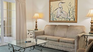 A living room with a beige sofa, a glass coffee table, two lamps, and a framed painting of birds on the wall. - Family Condo | 2 Kings, Loft | Great Location (Branson)
