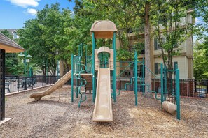 A playground with a slide and climbing structures, surrounded by trees and a fence. - Family Condo | 2 Kings, Loft | Great Location (Branson)