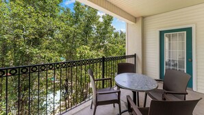 A balcony with a table and chairs, a door with a window, and a view of trees. - Spacious Family Condo | 2 Kings + Loft (Branson)