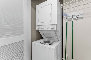 Ein kleiner Waschbereich mit einer Frontlader-Waschmaschine und einem Trockner, einem Wäscheständer und einem an der Wand befestigten Handtuchhalter.