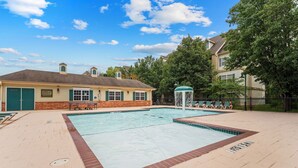 A swimming pool with a water fountain, lounge chairs, and a building with a brick facade. - Spacious Family Condo | 2 Kings + Loft (Branson)