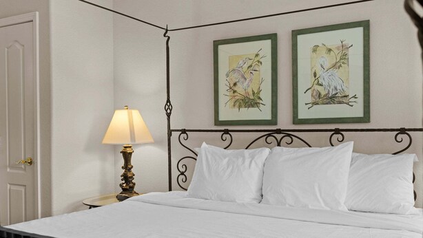 Cama com lençóis brancos, luminária de cabeceira e duas fotos emolduradas na parede.