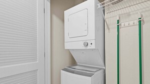 A front view of a white washing machine with a control panel, a door, and a green hose. - French Quarter Resort | Family Condo Near Shows (Branson)