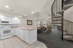 A spacious kitchen with white cabinetry, a central island, and a modern staircase leading to a living area. - French Quarter Resort | Family Condo Near Shows (Branson)