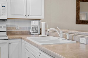 A kitchen with white cabinets, a coffee maker, a sink, and a microwave. - French Quarter Resort | Family Condo Near Shows (Branson)