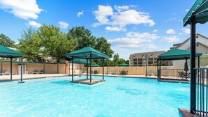 A swimming pool with multiple gazebos, lounge chairs, and a wooden fence. - French Quarter Resort | Family Condo Near Shows (Branson)